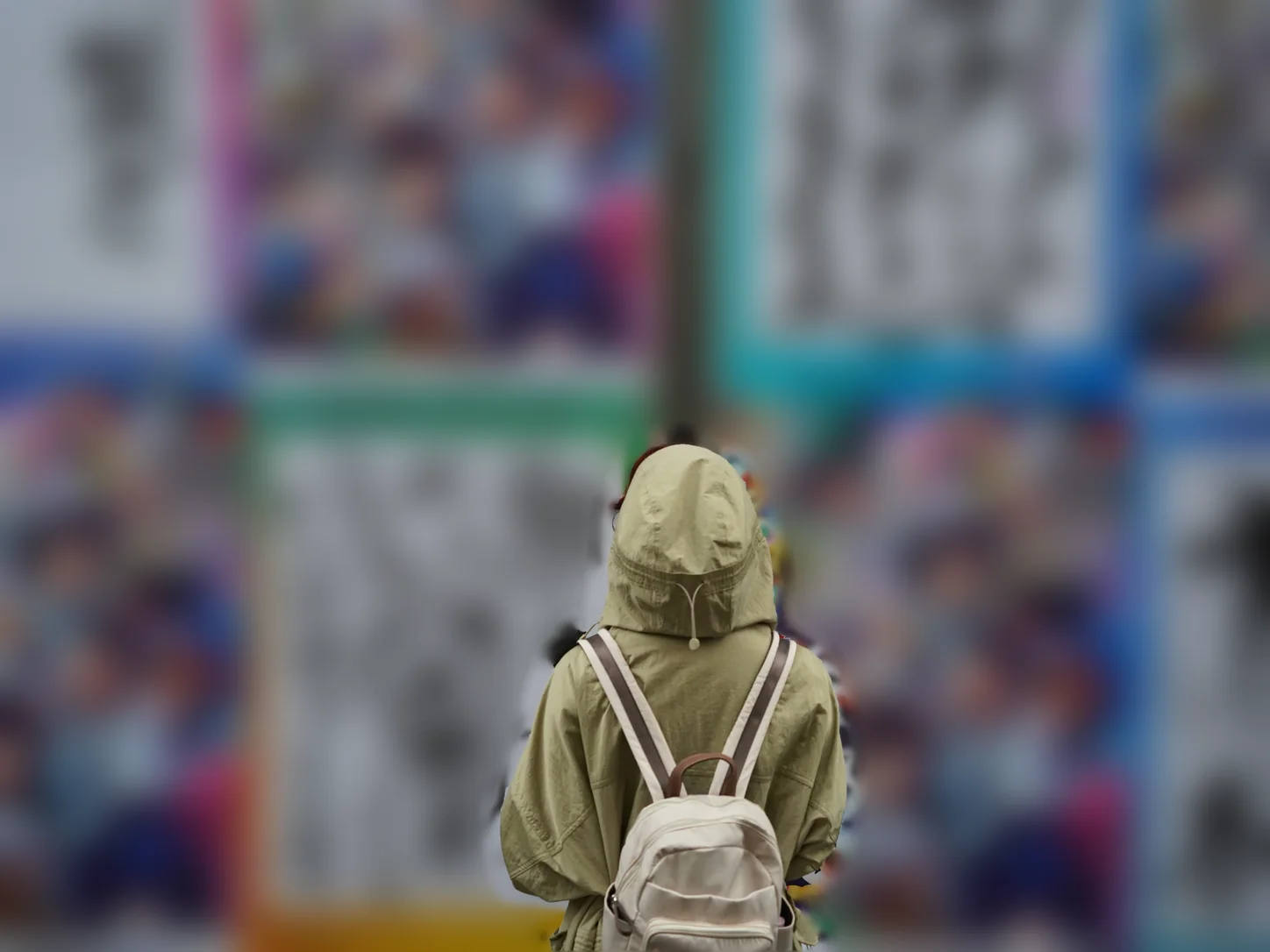 Person mit Rucksack vor einer Wand voller Plakate, die Plakate sind bewusst unscharf
