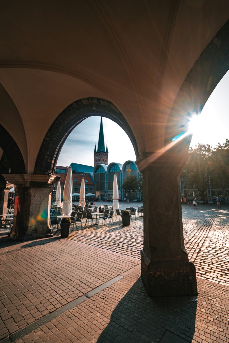Blick durch die Arkaden am Lübecker Markt auf Kopfsteinpflaster und Kirchturm im Gegenlicht