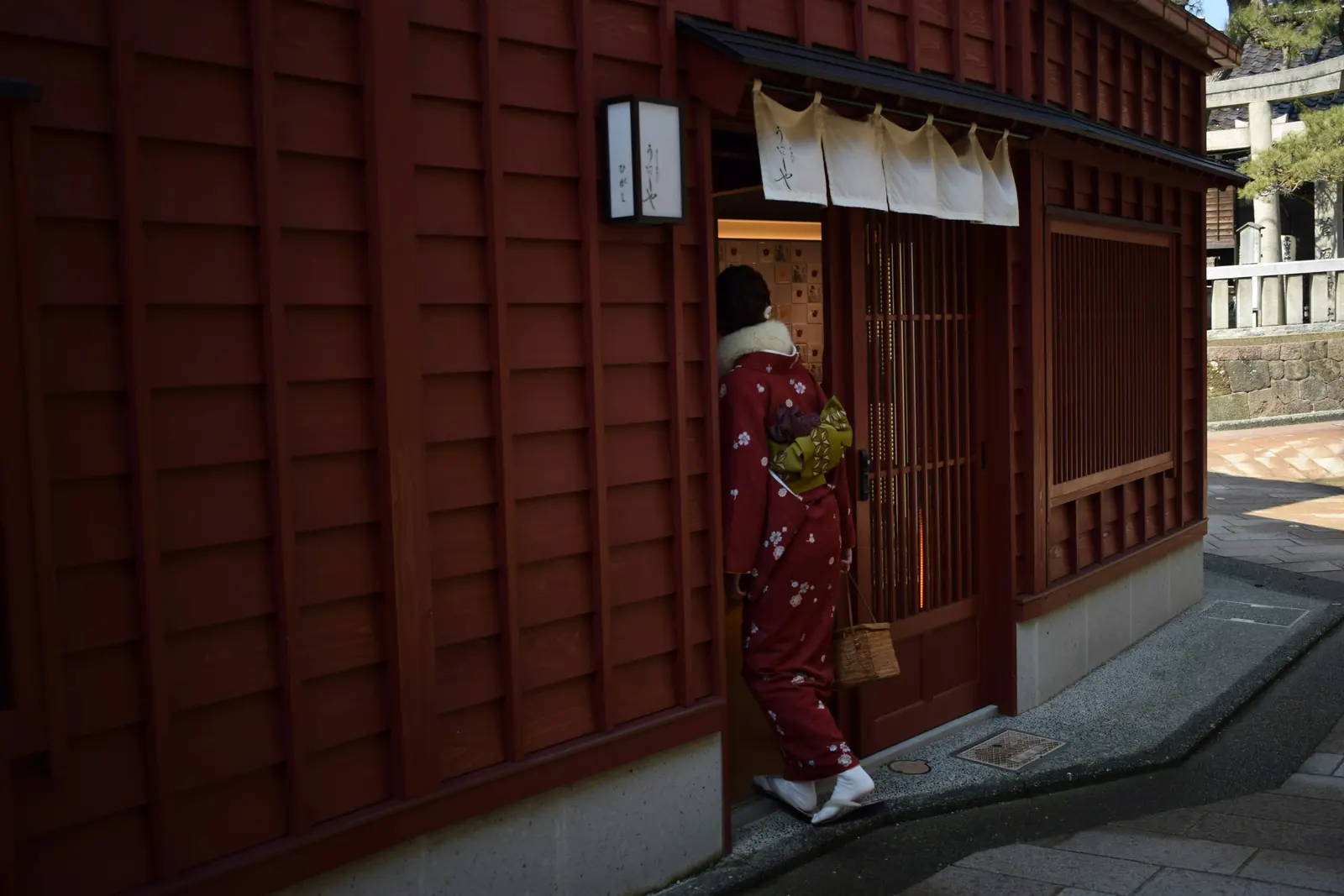 Foto: eine Person im roten Kimono tritt durch die offene Schiebetür eines traditionellen japanischen Ladens, drinnen warmes Licht: der Eingang in die Manga-&-Anime-Welt